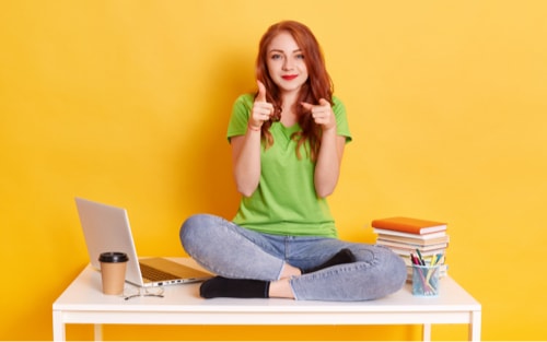 junge Frau sitzt im Schneidersitz auf einem Tisch mit Notbook und Büchern